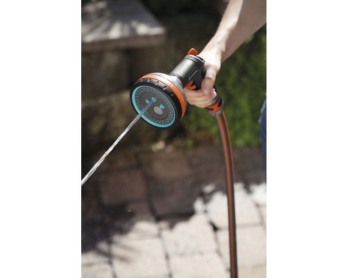 Ruka drží záhradný postrekovač, z ktorého vyteká voda.