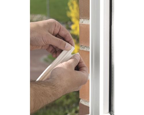 Osoba pripevňuje tesniacu pásku na rám okna, aby zabránila prievanu