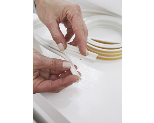 Ruky držia bielu ozdobnú lištu s lepiacou páskou