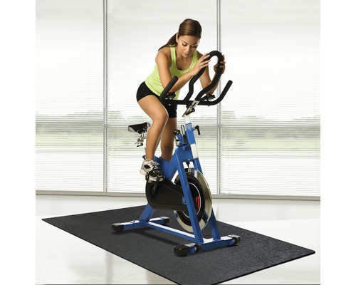 Žena cvičí na modrom spinningovom bicykli na čiernej podložke