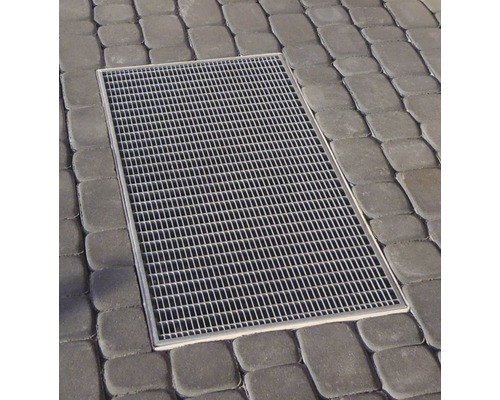 Pohľad zhora na obdĺžnikovú dvorovú vpusť s mriežkou, zasadenú do dlažobných kociek.