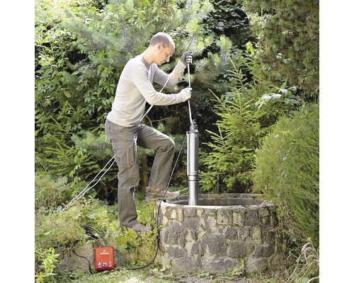 Muž inštaluje hlbinné čerpadlo do studne v záhrade.