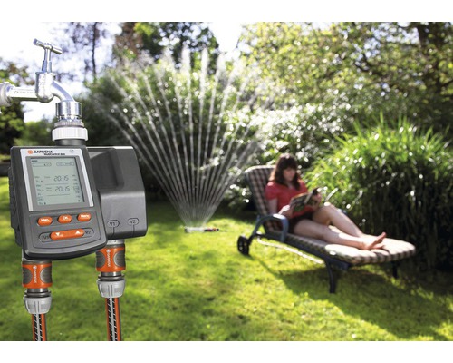Riadiaca jednotka zavlažovania Gardena s pripojením na vodovodný kohútik v záhrade so zavlažovačom trávnika a relaxujúcou ženou