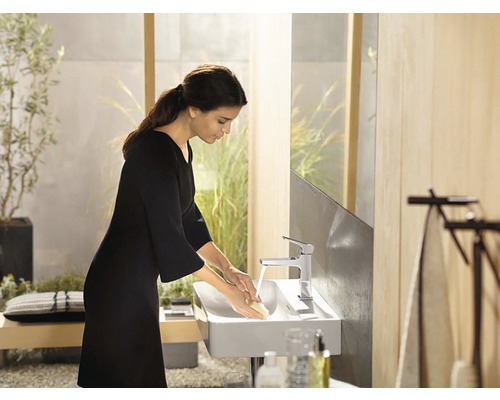 Žena si umýva ruky v modernej kúpeľni s umývadlom na dosku a vodovodnou batériou.