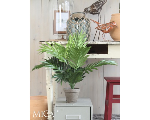 Dekoratívna umelá rastlina v kvetináči na príručnom stolíku, obklopená ďalšími dekoratívnymi prvkami.