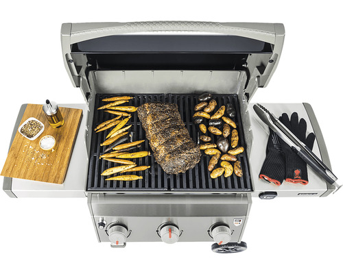 Plynový gril s mäsom a zeleninou na grilovacej mriežke, krájacia doska s korením, olejom a grilovacími kliešťami