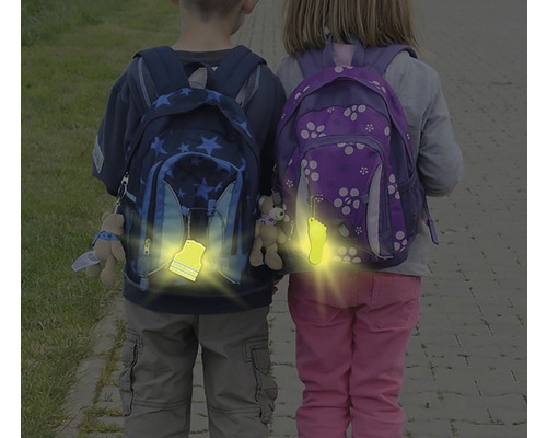 Dve deti so školskými batohmi a reflexnými príveskami na zvýšenie viditeľnosti v premávke