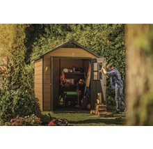 Záhradná scéna so záhradným domčekom, kde je uložené náradie a záhradnícke potreby, a muž rúbe drevo