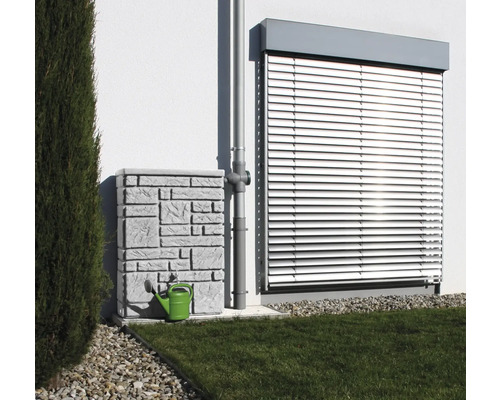 Nádrž na dažďovú vodu s kamenným vzorom a zelená kanva vedľa zvodu pred stenou domu