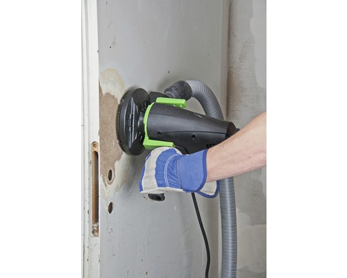 Remeselník brúsi stenu pomocou frézy na drážky v stene s odsávaním prachu