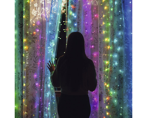 Žena stojí pred oknom s svetelnou reťazou Twinkly