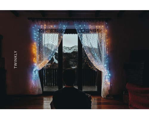 Osoba pred oknom so svetelným závesom Twinkly a výhľadom na hory