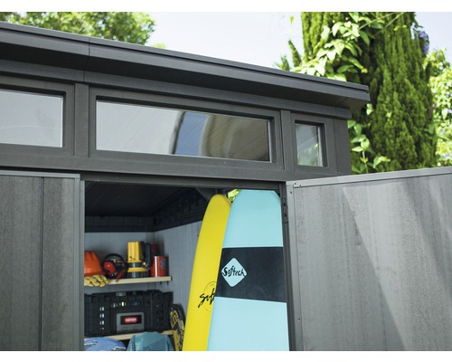 Záhradná búda s oknami a otvorenými dverami plná surfových dosiek a náradia.