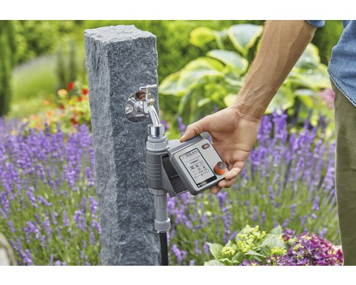 Riadiaca jednotka zavlažovania Gardena na vodovodnom kohútiku s osobou v záhrade.