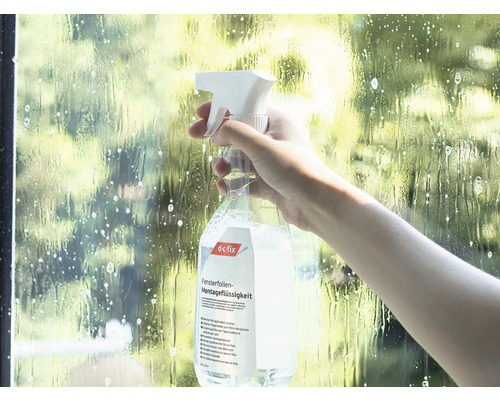 Osoba strieka montážnu kvapalinu na okenné fólie na okno.