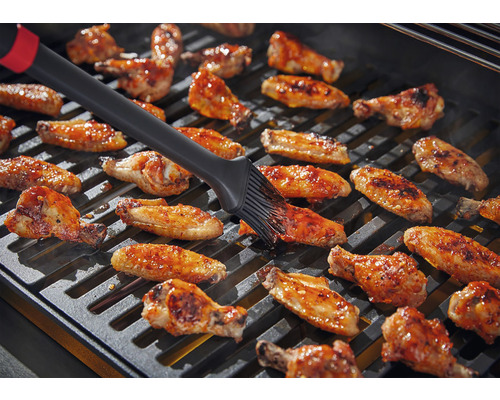 Kuracie krídelká sa potierajú štetcom na grile.