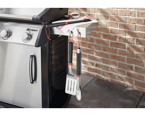 Plynový gril s grilovacím náčiním a uterákom pri tehlovej stene