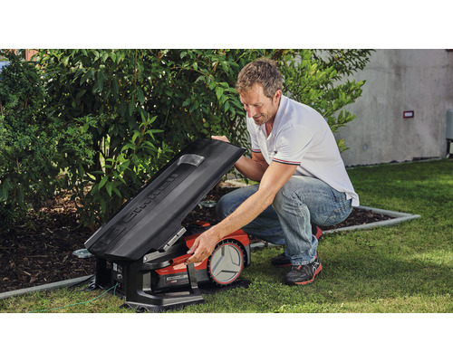 Muž otvára veko robotickej kosačky na trávu v záhrade.