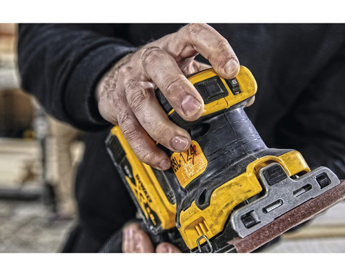 Detailný záber muža držiaceho excentrickú brúsku DeWalt.