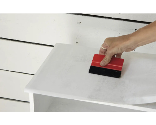 Aplikácia nábytkovej fólie stierkou na kus nábytku.