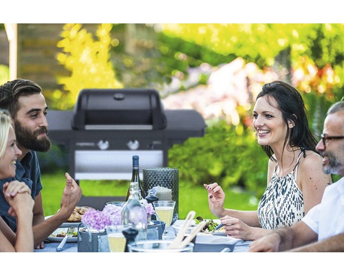 Záhradná scéna s ľuďmi pri stole a plynovým grilom