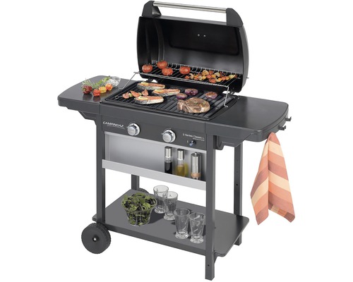 Plynový gril s grilovaným jedlom na rošte a odkladacími plochami.