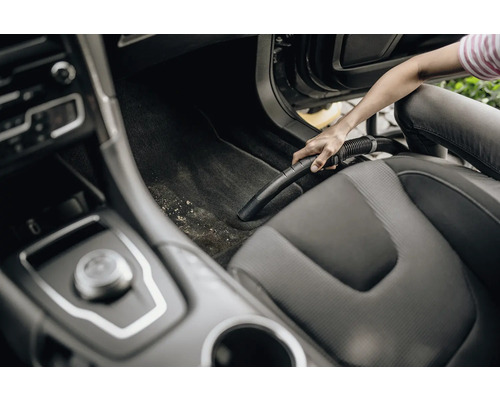 Osoba vysáva interiér auta vysávačom.