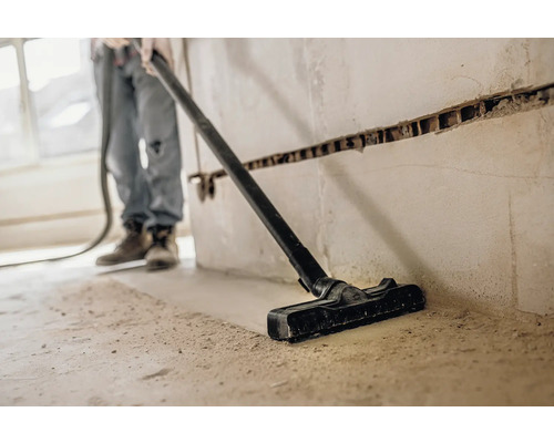 Osoba vysáva prach vysávačom na stavenisku.