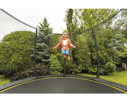Dievča skáče na záhradnej trampolíne so sieťou pred zelenými kríkmi