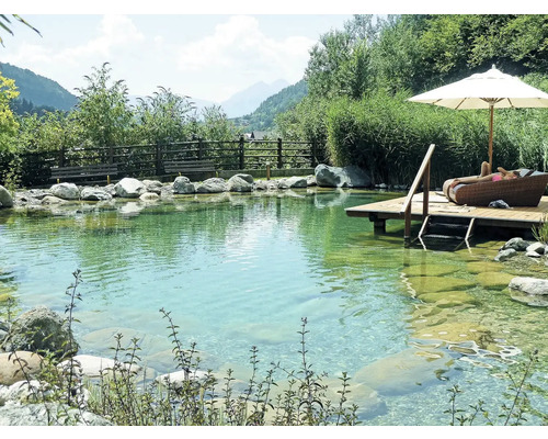 Prírodný bazén s drevenou terasou, lehátkom, slnečníkom a kameňmi na brehu