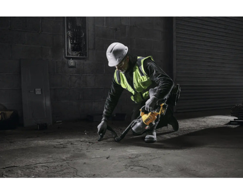 Muž s ochrannou helmou a výstražnou vestou používa priemyselný vysávač na betónovej podlahe.