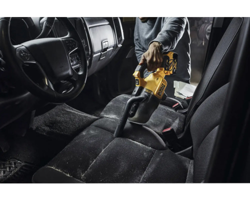 Osoba vysáva interiér auta žltým ručným vysávačom DeWalt.