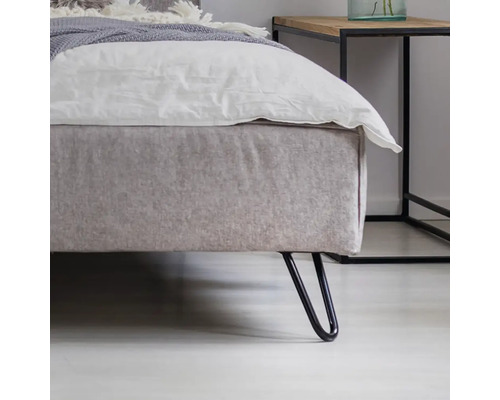 Detailný pohľad na posteľ boxspring so sivým čalúnením a čiernymi kovovými nohami vedľa nočného stolíka
