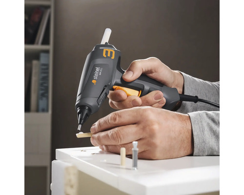 Osoba používa tavnú pištoľ Steinel na lepenie kusov dreva na biely povrch