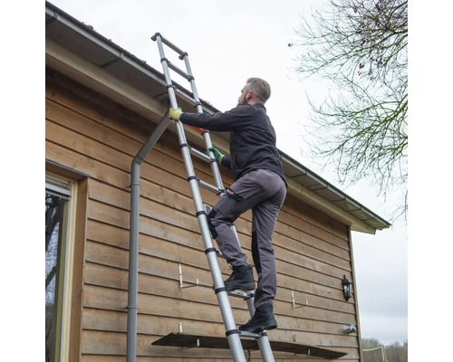 Osoba stúpa po teleskopickom rebríku na stene domu.