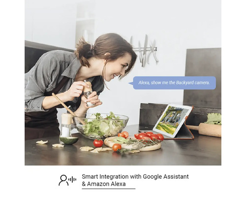 Žena pripravuje šalát v kuchyni a používa tablet s hlasovým ovládaním pre bezpečnostnú kameru