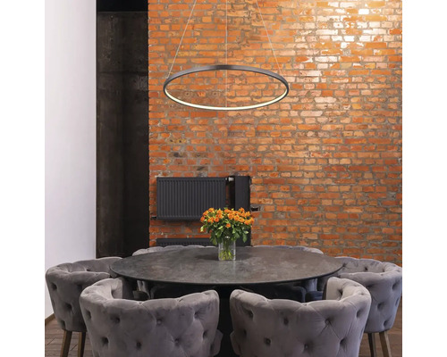 Scéna s kruhovým závesným svietidlom nad jedálenským stolom so stoličkami pred tehlovou stenou