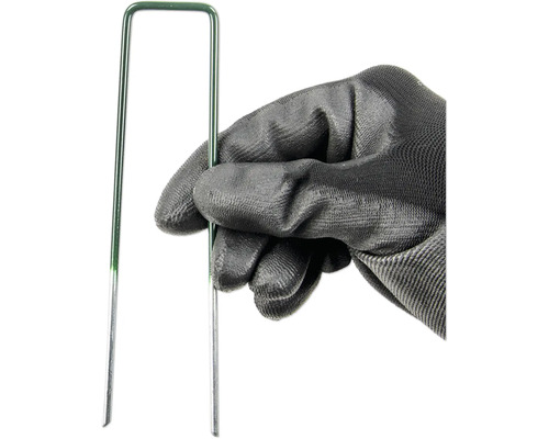 Ruka v záhradnej rukavici drží zelený trávnikový klinec.