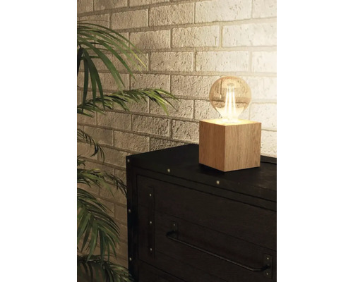 Stolná lampa s drevenou základňou a žiarovkou na komode pred tehlovou stenou