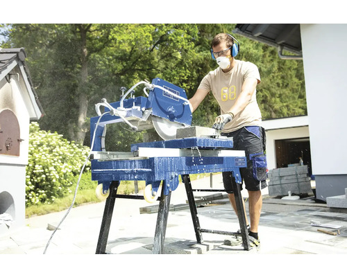 Muž používa vonkajšiu pílu na kameň, vybavenú ochranou sluchu a protiprachovou maskou.