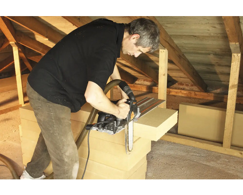 Muž reže izolačné dosky reťazovou pílou v podkroví.