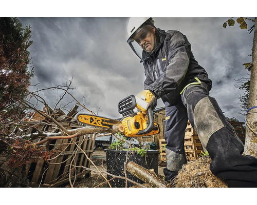 Muž s ochrannými pomôckami používa reťazovú pílu DeWalt na prerezávanie konárov.