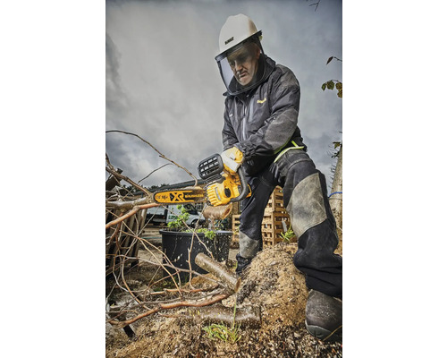 Muž s ochrannou prilbou a tvárovým štítom pília konáre motorovou pílou.