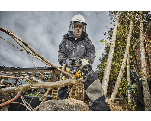 Osoba v ochrannom odeve a prilbe reže konár akumulátorovou pílou. V pozadí sú vidieť stromy.